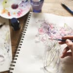 An artist using watercolours to paint a vase of flowers