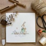 A greetings card showing a family of rabbits watering their carrot patch